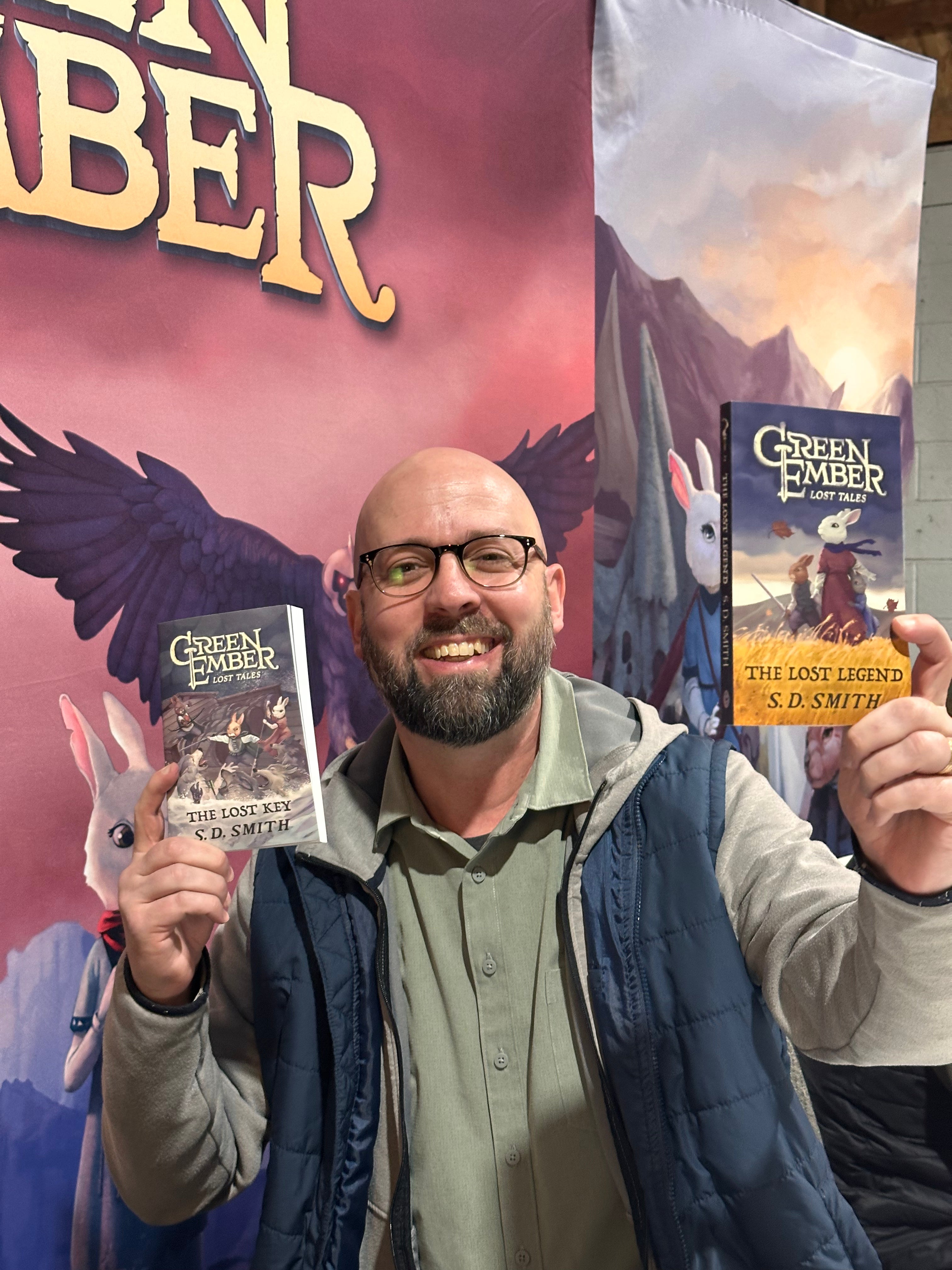 Man holding 'Green Ember' books in front of a colorful book cover display
